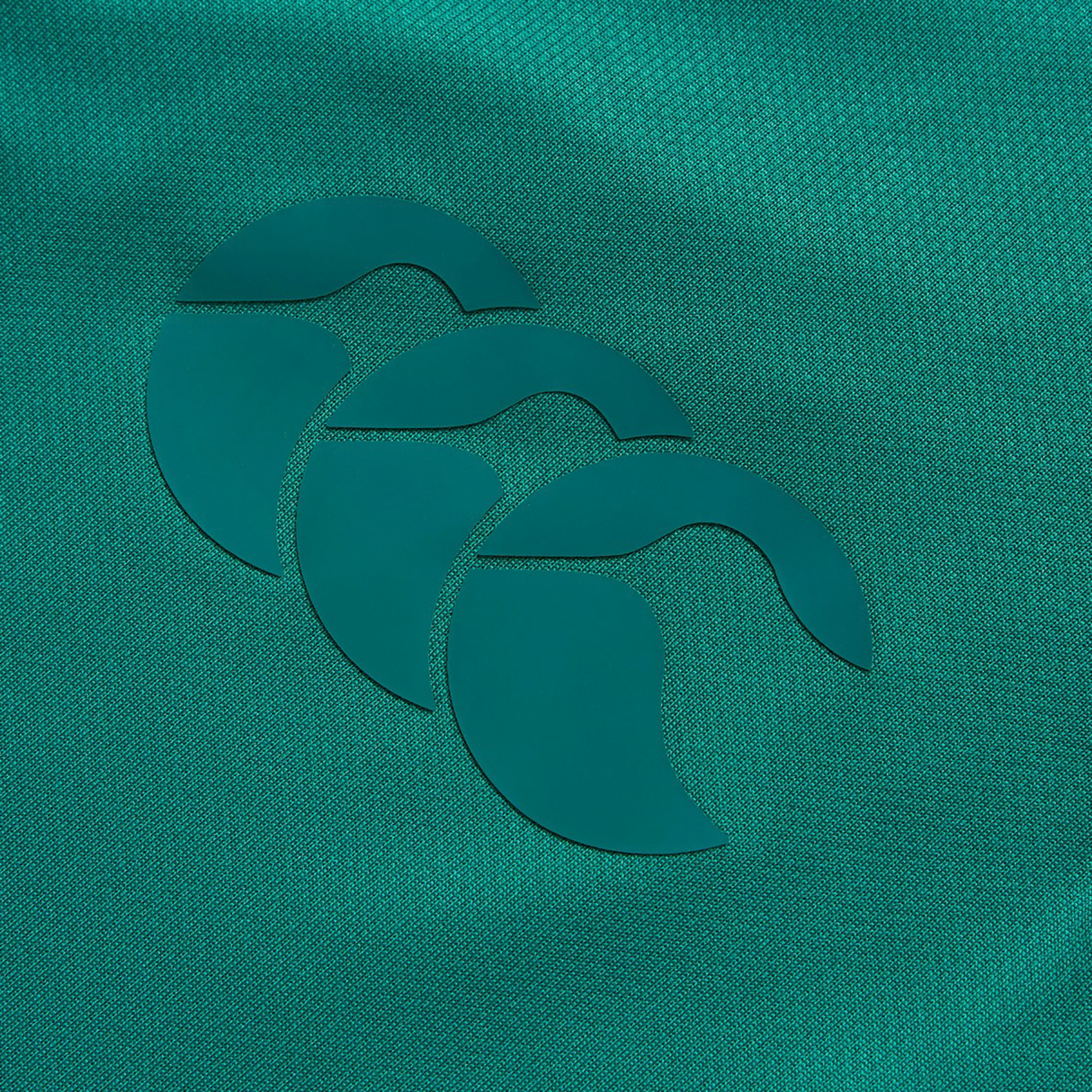 Three overlapping teal crescent shapes on a textured teal background capture the dynamic spirit of Ireland Rugby, akin to the innovative design featured in the Ireland 150th Anniversary Pro Home Jersey by Canterbury with Vapodri Technology.