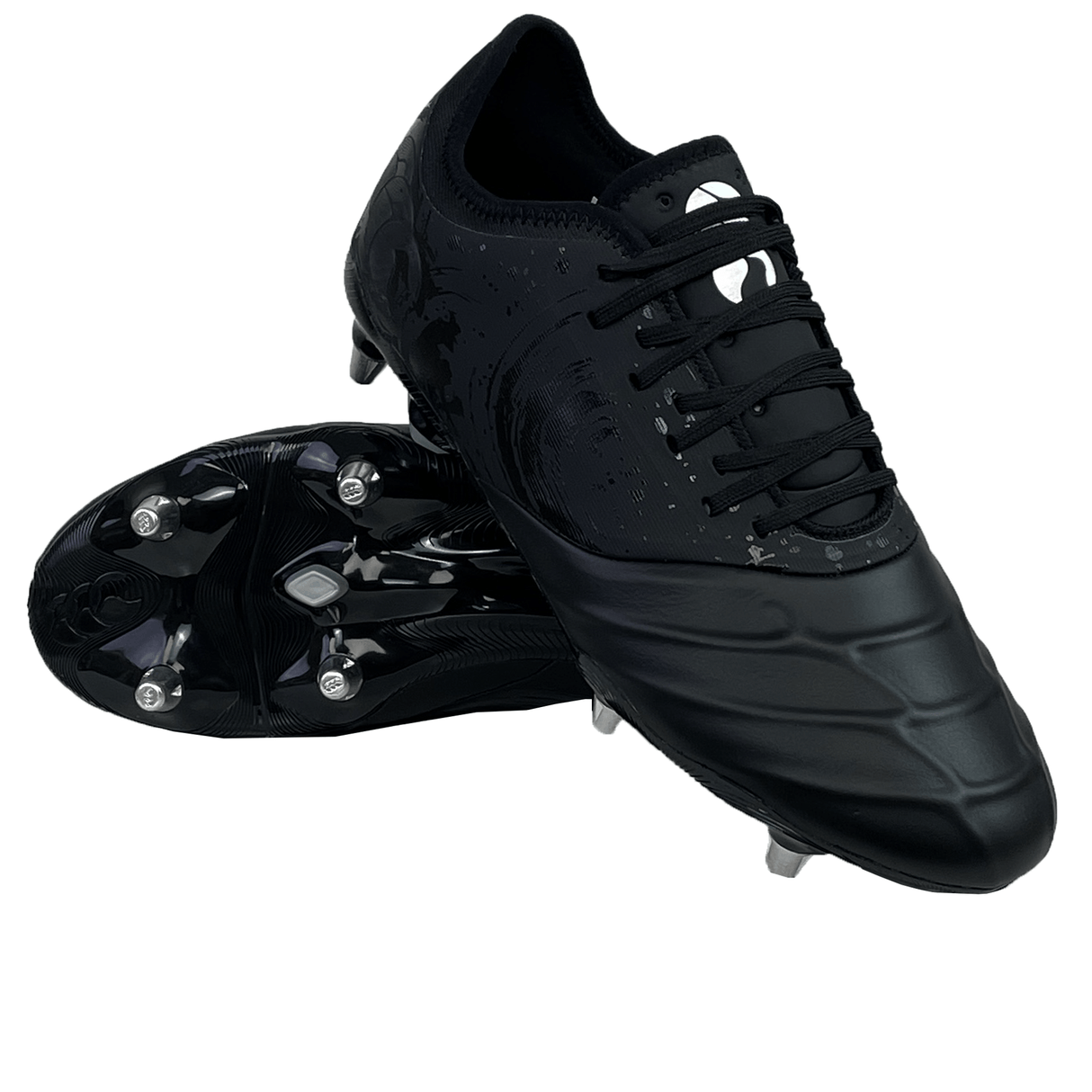 A pair of black Canterbury Phoenix Genesis Pro SG soccer cleats, one lying on its side showcasing the metal studs on the sole for optimal traction, and the other standing upright. These soft ground boots are ideal for enhancing performance on the field.