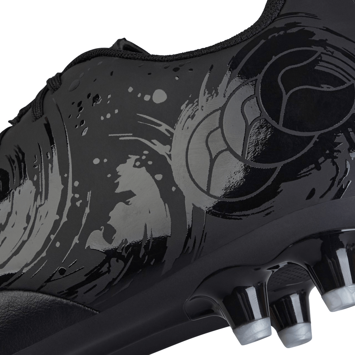 Close-up image of the black Canterbury Phoenix Genesis Team FG soccer cleat featuring a textured synthetic leather forefoot with circular motifs and spiked studs on the firm ground boot's outsole in silver metallic.