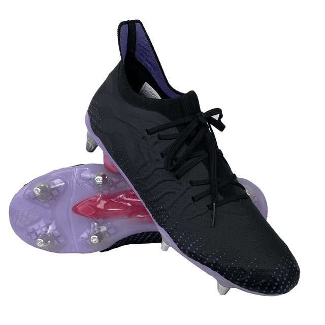 A pair of Canterbury Speed Infinite Elite SG soccer cleats in Black/Verbena with metal studs on the soles, featuring lightweight stability and VAPOSKIN membrane, shown with one shoe placed on top of the other.