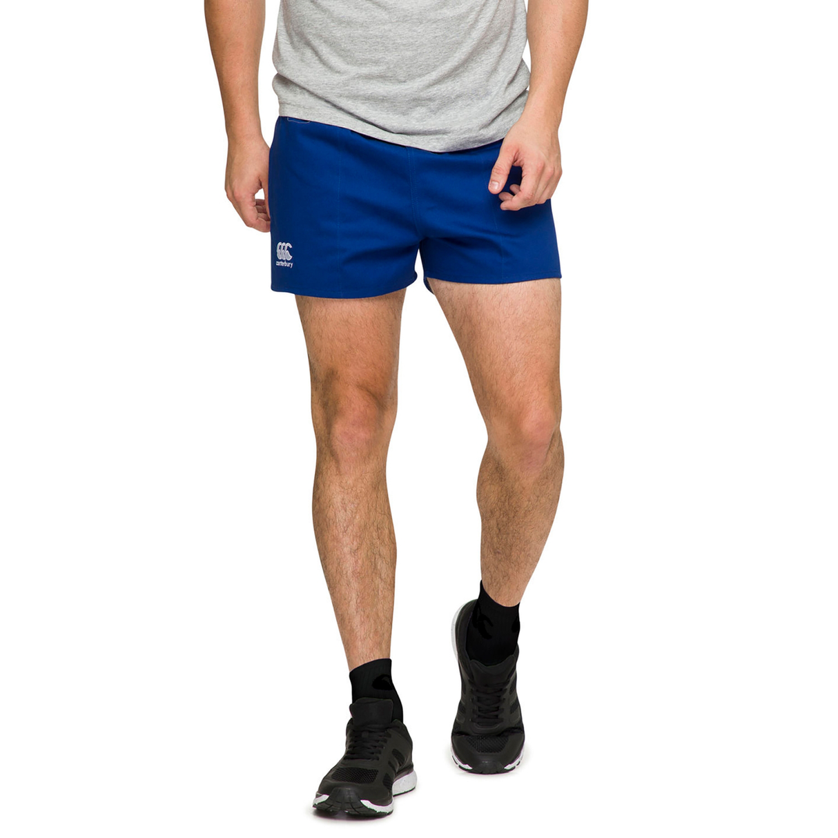 A person in a gray t-shirt, Canterbury's Rugged Drill Shorts in blue, and black sneakers stands against a white background.