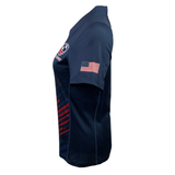 Side view of the Women's USA Rugby Pro Home Jersey by Castore in navy blue with an American flag patch on the sleeve and logo on the chest. It has an athletic fit with red and white accents on the lower half, crafted from moisture-wicking fabric for comfort.