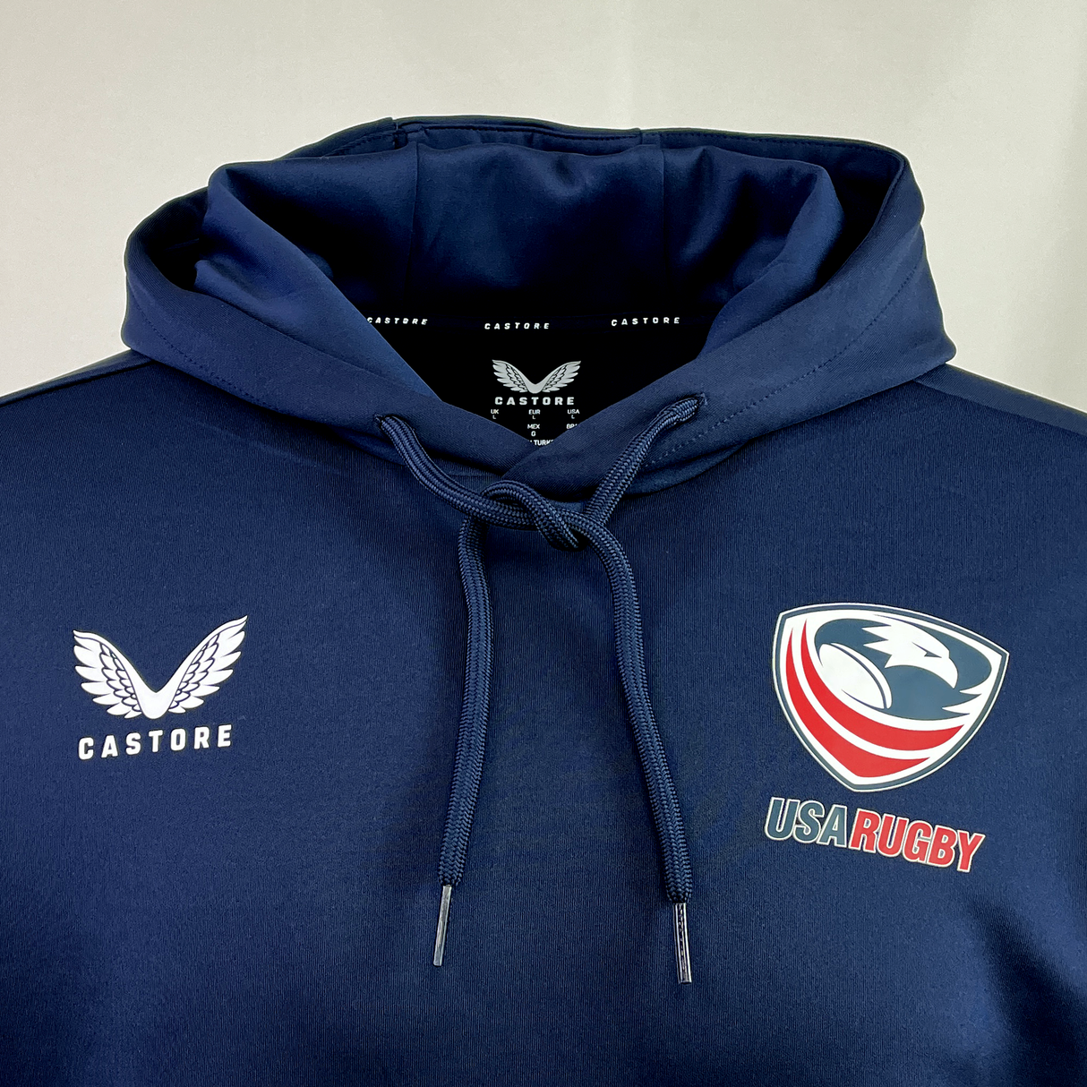 Introducing the USA Rugby Hoodie by Castore, a stylish blue hoodie made from premium polyester, showcasing the renowned "Castore" branding along with the USA Rugby logo.