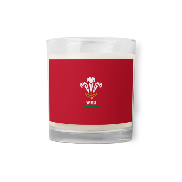 Clear glass candle holder with a red label featuring a white and green emblem and the text "WRU." An essential addition to any rugby fan's collection, the PF LIC Wales Rugby Soy Wax Candle is also environmentally friendly.