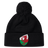 The EMB Canterbury Wales Shield Pom Pom Beanie is a stylish black beanie with a striking patch featuring a red dragon against a green and white backdrop, reminiscent of the Wales Shield.