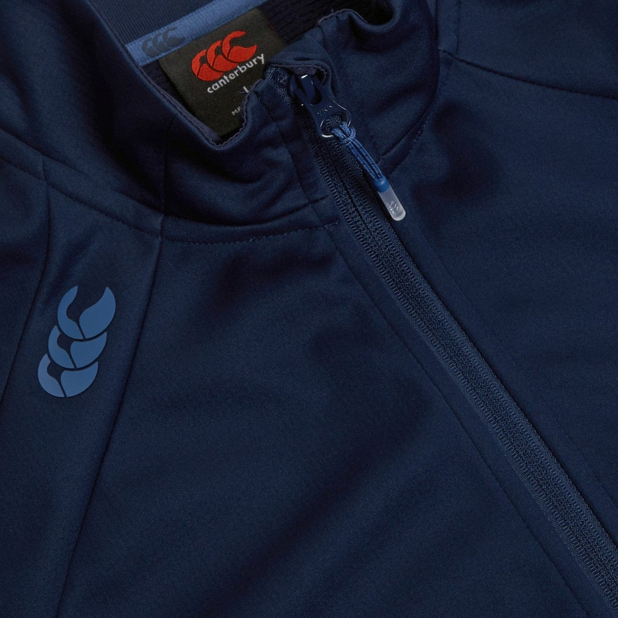 Close-up of a navy blue Canterbury Elite Windstopper jacket with a logo on the left side and a zipper detail.