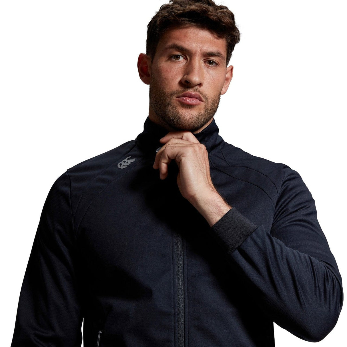 Man with light skin and short curly hair wearing a Canterbury Elite Windstopper Jacket, posing with his hand on his chin, on a white background.