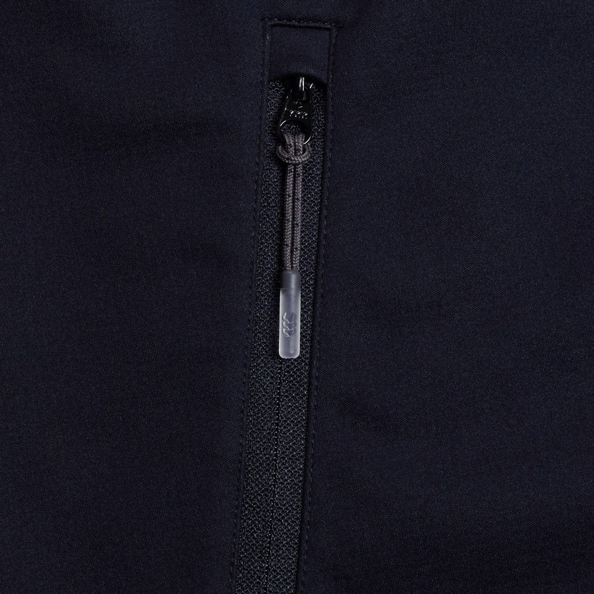 Close-up of a black zipper on the Canterbury Elite Windstopper Jacket, showing the metal puller with a logo engraved.