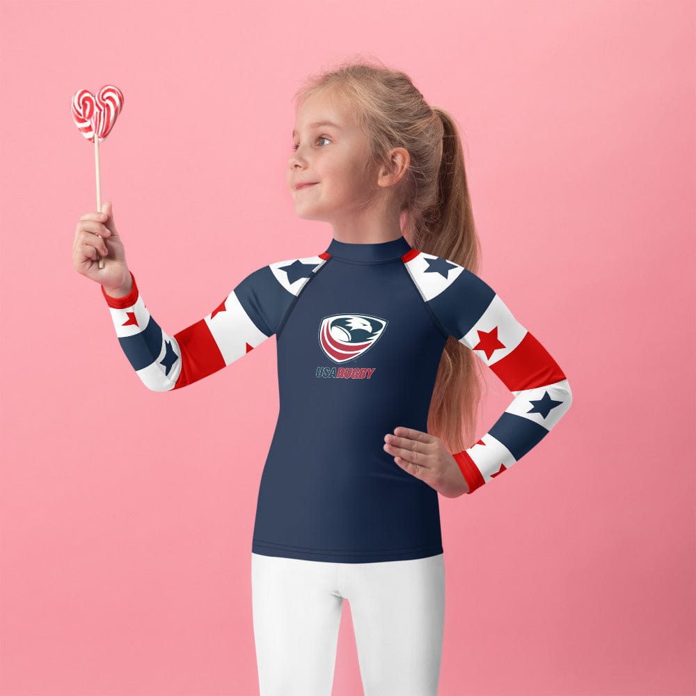 Girl wearing a Long sleeve rash guard with a red, white and blue stars and stripes design on the sleeves, a navy body and a USA Rugby logo center front.