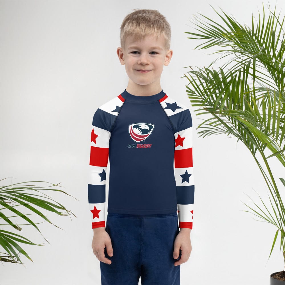 Boy wearing a Long sleeve rash guard with a red, white and blue stars and stripes design on the sleeves, a navy body and a USA Rugby logo center front.