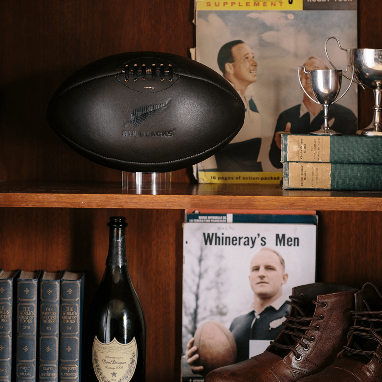 A book shelf with a bottle of wine and an All Blacks Vintage Leather Ball by Gilbert.