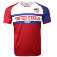 Round neck short sleeve jersey with white chest and upper left American flag in corner. Red right shoulder and sleeve and blue left shoulder and sleeve trimmed in red. Two horizontal blue stripes run across the chest. United States centered in red on the white jersey with Rugby in white on the blue stripe. The lower torso is red.