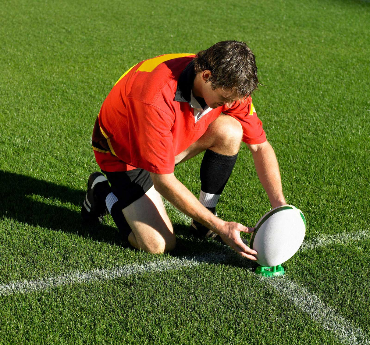 a man kneeling down on top of a field holding a Gilbert Kicking Tee Green 320 Precision.