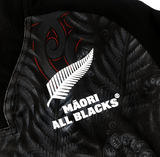 Close-up of the Māori All Blacks Home Supporters Jersey by adidas, made from moisture-wicking fabric and showcasing a white fern along with stylized black and red patterns.