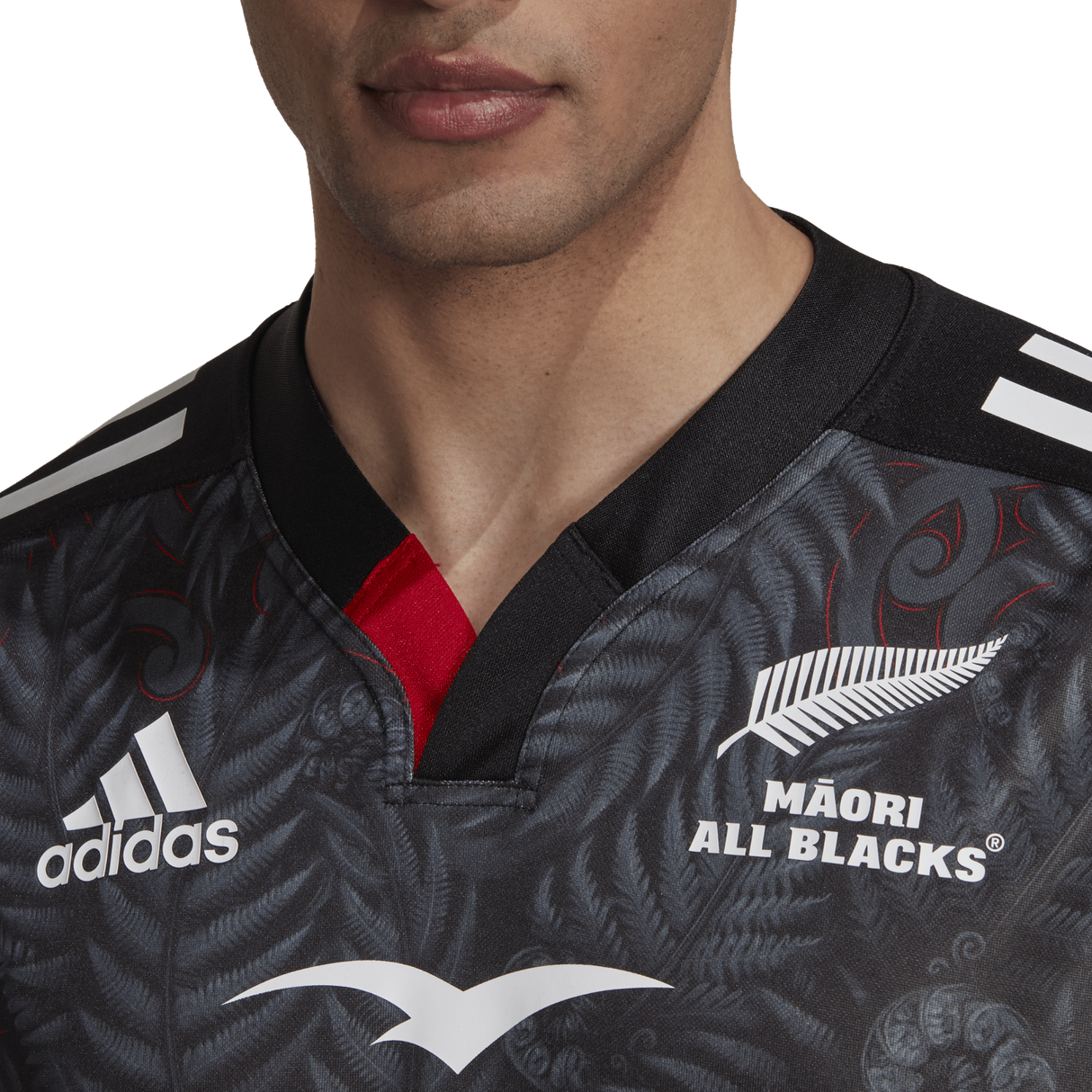 Wearing the adidas Māori All Blacks Home Supporters Jersey in black, a person proudly displays the white logos and intricate patterns on this moisture-wicking garment.